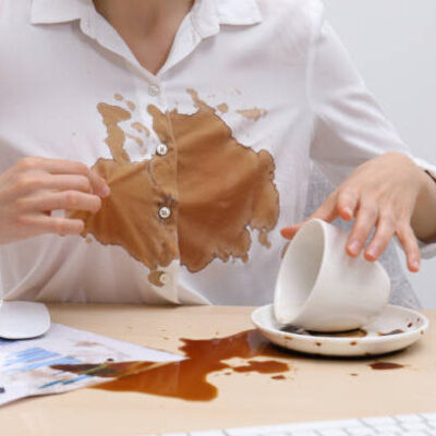 Woman in dirty shirt at wooden desk with coffee spill, closeup